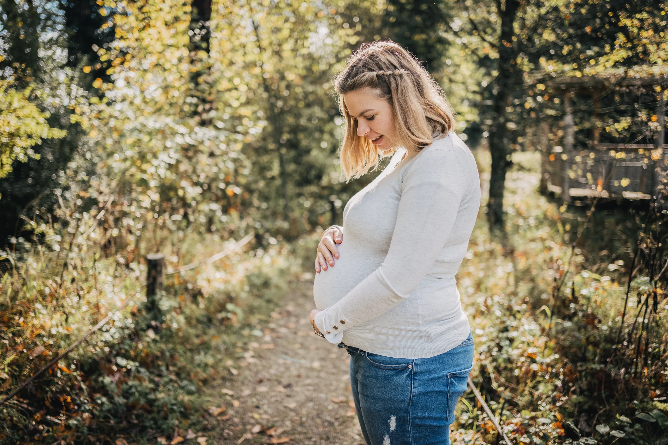 Schwangere Frau in natürlicher Umgebung, liebevoll ihren Babybauch haltend