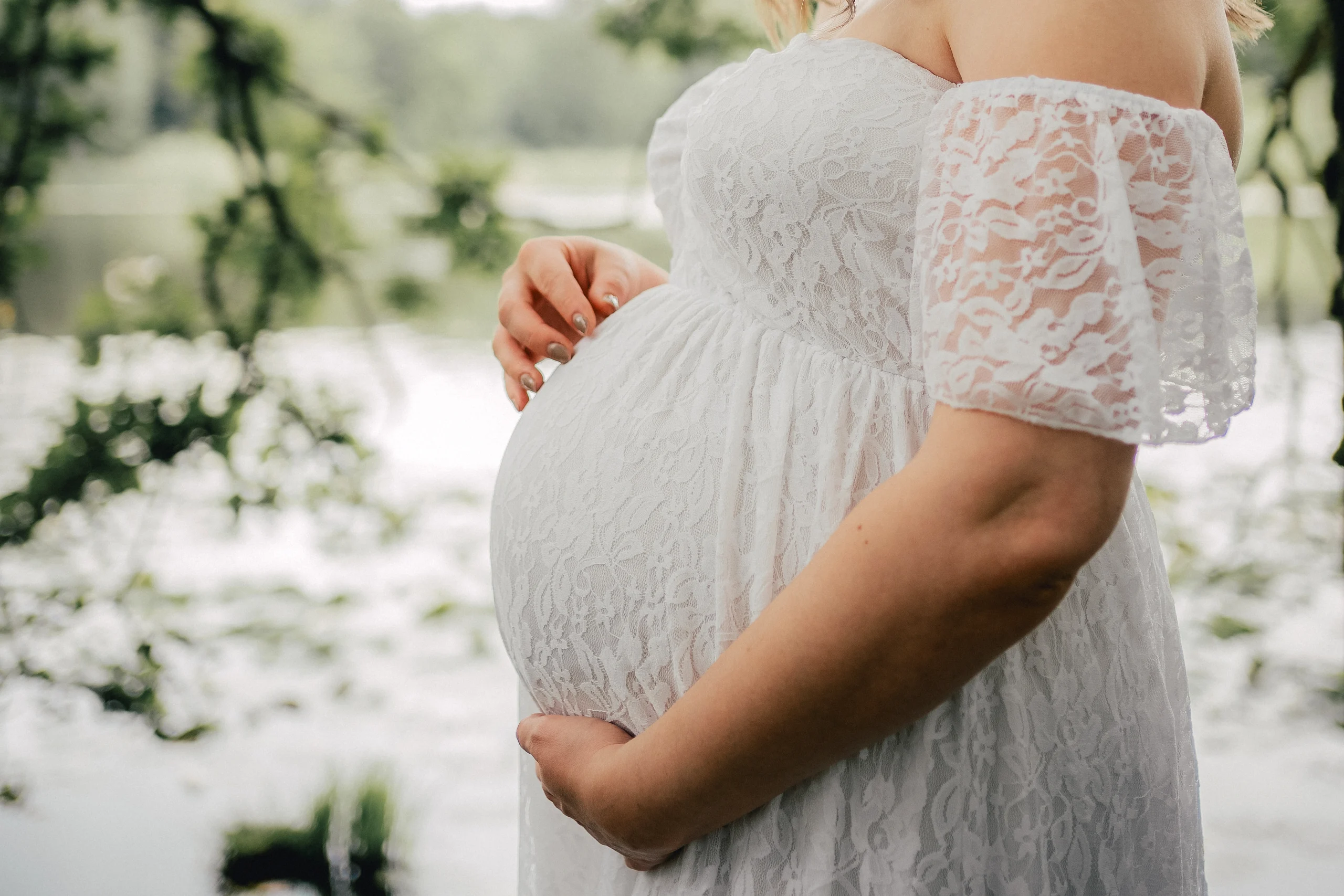 Nahaufnahme des Babybauchs einer schwangeren Frau, umrahmt von den Händen ihrer Familie