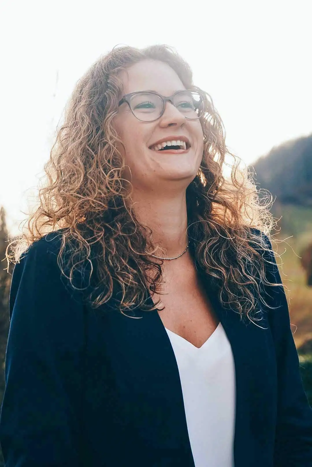 Lachend mit blonden Locken ist die Frau auf dem Foto zu sehen.